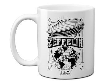 May include: White ceramic mug featuring a black and white graphic of a zeppelin airship, a globe, and the text "Zeppelin Round the World Flight 1929 August 8-29".