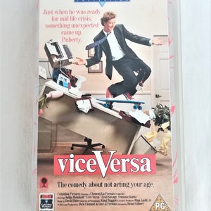 May include: A VHS tape cover for the comedy film "Vice Versa" starring Judge Reinhold and Fred Savage. The cover features a photo of Judge Reinhold skateboarding in an office setting. The text on the cover reads "The comedy about not acting your age."