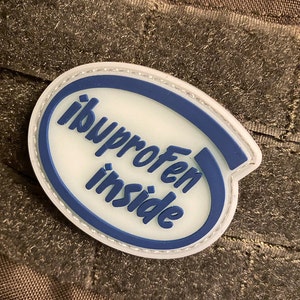 Puede incluir: Un parche ovalado blanco con un borde azul y el texto "ibuprofeno inside" en letras azules.