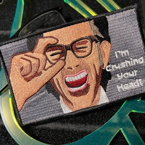May include: Embroidered patch featuring a man with glasses smiling and making a hand gesture. The text "I'm crushing your heads" is written in white on a gray background.