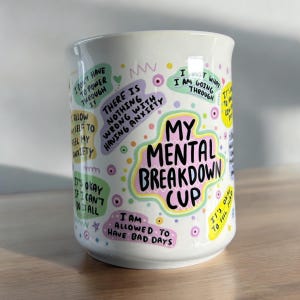 Könnte beinhalten: Eine weiße Keramiktasse mit buntem Text und Illustrationen. Der Text lautet "My Mental Breakdown Cup" und enthält Sätze wie "Ich muss nicht durchziehen", "Es ist nichts falsch daran, Angst zu haben" und "Ich darf schlechte Tage haben".