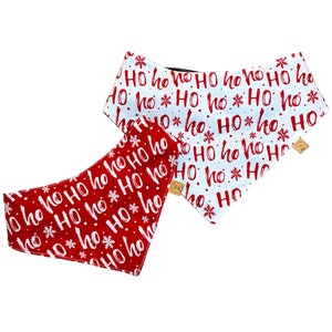 May include: Two dog bandanas with a Christmas theme. One is red with white "Ho Ho Ho" text and snowflakes. The other is white with red "Ho Ho Ho" text and snowflakes. Both have wooden button closures.