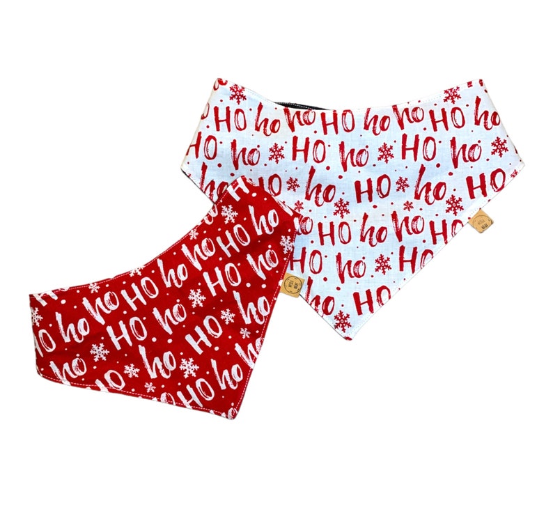 May include: Two dog bandanas with a Christmas theme. One is red with white "Ho Ho Ho" text and snowflakes. The other is white with red "Ho Ho Ho" text and snowflakes. Both have wooden button closures.