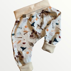 Puede incluir: Un pantal&oacute;n de beb&eacute; con fondo azul claro y un patr&oacute;n de b&uacute;hos, castillos y otras im&aacute;genes con tem&aacute;tica de Harry Potter. El pantal&oacute;n tiene un pu&ntilde;o beige en la cintura y los tobillos.