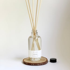 May include: A clear glass bottle with a white label that reads "C.L.O. Lavender Reed Diffuser 14.8 fl oz" and natural wooden sticks in the bottle. The bottle is sitting on a wooden slice.