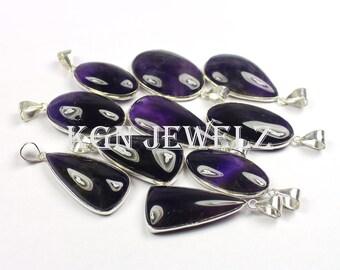 May include: A collection of ten amethyst gemstone pendants with silver bail settings. The pendants are various shapes and sizes, with some being oval and others being teardrop shaped. The amethyst is a deep purple color.