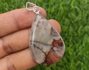 May include: A teardrop-shaped pendant with a silver bail. The pendant features a polished stone with a mix of beige, brown, and red hues, and dark veins. The stone is set in a silver bezel.
