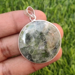 May include: A round green and white gemstone pendant with a silver bail. The pendant is set in a silver frame.