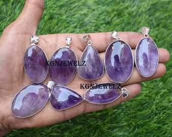 May include: Eight amethyst gemstone pendants with silver settings. The pendants are various shapes and sizes, including oval, teardrop, and round. The amethyst is a deep purple color.