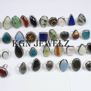 May include: A collection of 28 silver rings with various gemstone settings. The rings feature a variety of colors and shapes, including blue, green, red, and black. The rings are all set in silver and have a delicate, ornate design.