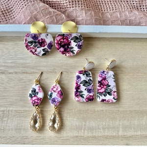 May include: Three pairs of floral print earrings. The first pair is a semi-circle shape with gold accents. The second pair is a rectangle shape with gold accents. The third pair is a teardrop shape with a clear crystal and gold accents.