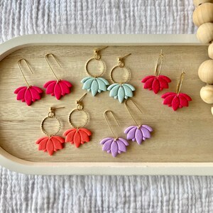 May include: A set of six pairs of earrings featuring a flower design. The earrings are made of gold metal and have a variety of colors, including pink, purple, green, and orange.