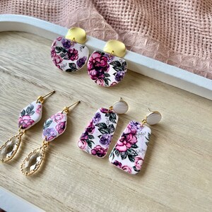 May include: A set of four floral patterned earrings with gold and white accents. The earrings are displayed on a wooden surface.