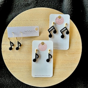 May include: Three pairs of black music note earrings on white cards with gold hooks. The cards have the text "Seize The Clay Jewelry" and a website address.