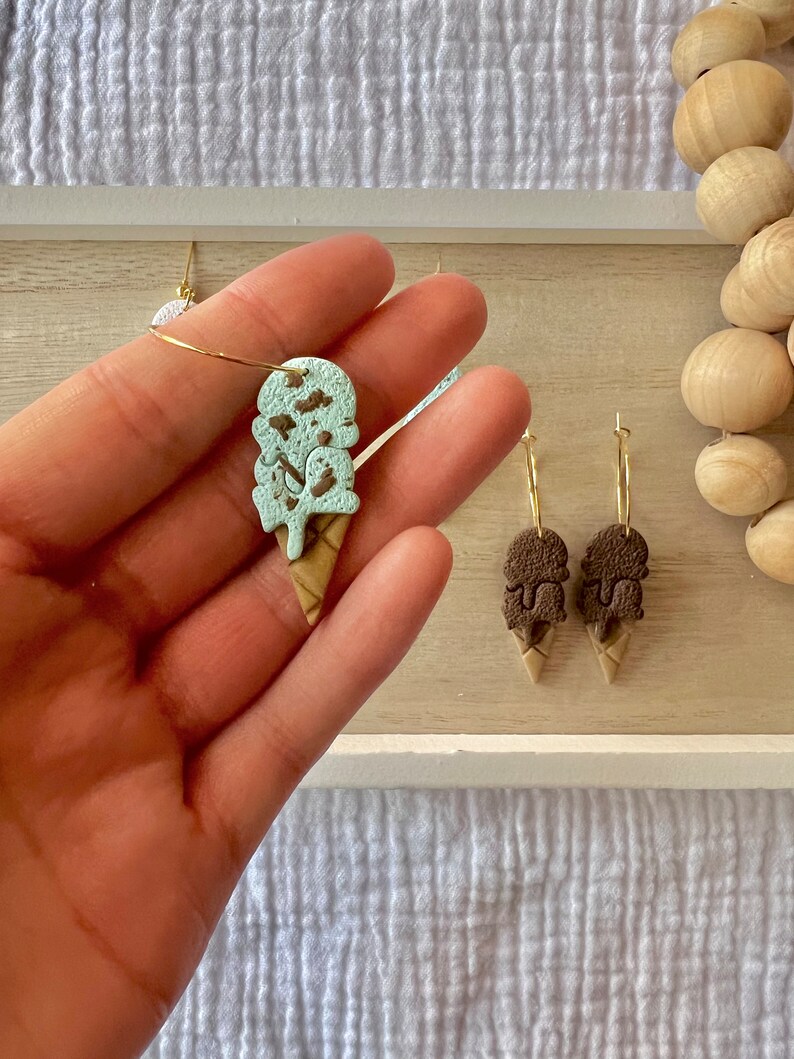 May include: A pair of gold hoop earrings with ice cream cone charms. One charm is mint green with brown sprinkles and the other is brown with white sprinkles.