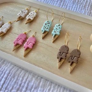 May include: A set of six pairs of ice cream cone earrings. The earrings are made of polymer clay and come in four different flavors: chocolate, vanilla, strawberry, and mint chip. The earrings are available in both stud and hoop styles.