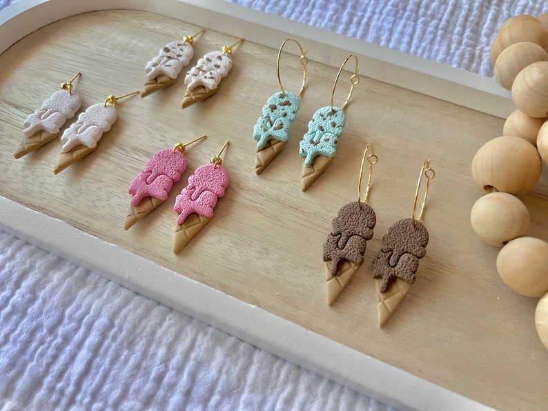 May include: A set of six pairs of ice cream cone earrings. The earrings are made of polymer clay and come in four different flavors: chocolate, vanilla, strawberry, and mint chip. The earrings are available in both stud and hoop styles.