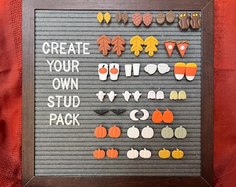 May include: A felt board with various fall-themed stud earrings. Designs include leaves, acorns, owls, pumpkins, ghosts, bats, and coffee cups. The text "CREATE YOUR OWN STUD PACK" is displayed in white letters.