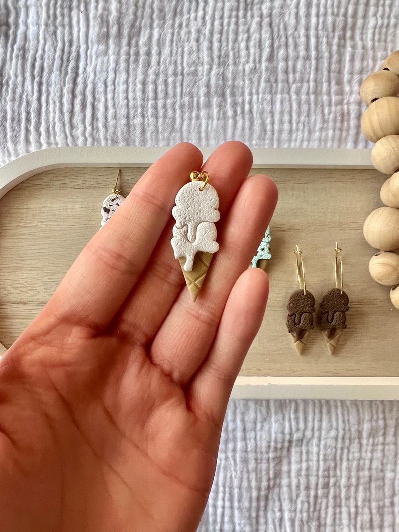 May include: White and brown ice cream cone shaped earrings with a gold accent. The earrings are made of polymer clay and are handmade.
