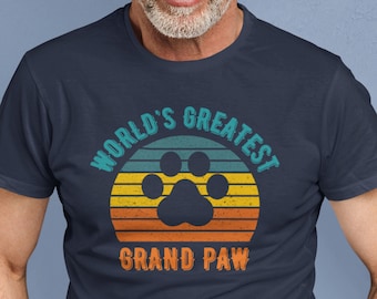 Op de afbeelding: Een marineblauw t-shirt met een vintage-stijl grafische afbeelding met de tekst "World's Greatest Grand Paw" met een pootprint en een zonsondergangontwerp.