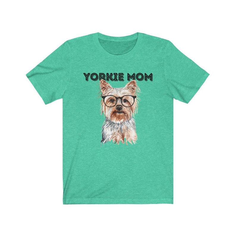 May include: A teal green t-shirt with the text "Yorkie Mom" in black lettering. A watercolor illustration of a Yorkshire Terrier wearing glasses is centered on the shirt.