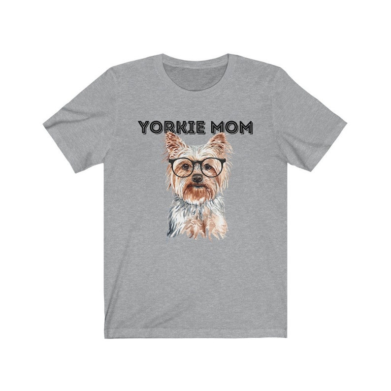 May include: A heather grey t-shirt with the text "Yorkie Mom" printed in black. A watercolor illustration of a Yorkshire Terrier wearing glasses is centered on the shirt.