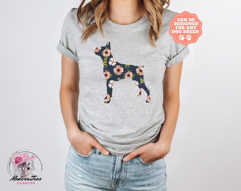Puede incluir: Una camiseta gris con una silueta de perro con estampado floral. El texto "Se puede dise&ntilde;ar para cualquier raza de perro" est&aacute; en un c&iacute;rculo rosa en la esquina superior derecha de la imagen.