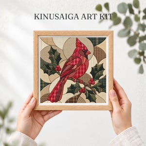 Op de afbeelding: Een Kinusaiga-kunstset met een vierkante houten lijst met een stoffen collage van een rode kardinaalvogel op een tak met groene hulstbladeren en rode bessen, tegen een achtergrond van geometrische vormen in beige en bruin ruitpatroon.