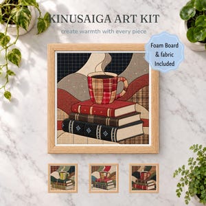 Può includere: Un kit artistico Kinusaiga con un'immagine quadrata incorniciata di una tazza da caffè a quadri appoggiata su una pila di tre libri. Il kit include pannello in schiuma e tessuto. Il testo recita KINUSAIGA ART KIT, create warmth with every piece e Foam Board & fabric Included.