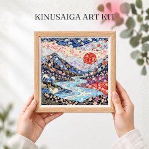 May include: A Kinusaiga art kit featuring a framed fabric collage of a landscape with mountains, a winding river, and a large red sun. The scene is decorated with floral patterns in blue, red, pink, and gold, all encased in a light wood frame.
