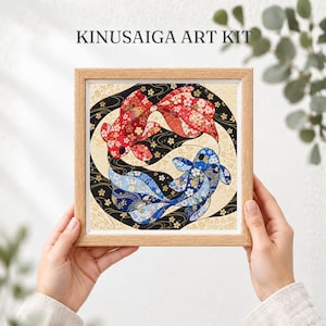 以下が含まれることがあります： KINUSAIGA ART KITと書かれた木製フレーム入りのアートキット。布地で作られた赤と青の2匹の鯉が描かれており、それぞれに花柄があしらわれ、黒とクリーム色の背景に配置されています。