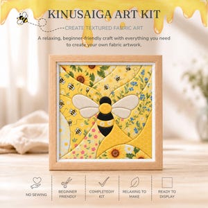 May include: A Kinusaiga art kit featuring a square wooden frame containing a fabric collage of a central bee surrounded by sunflowers, small blue flowers, and honeycomb patterns. The text reads Kinusaiga Art Kit, Create Textured Fabric Art.