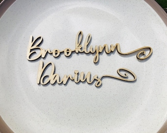 May include: Two wooden names, "Brooklyn" and "Darius", are written in cursive script on a white plate.
