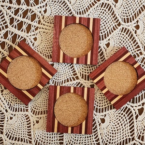 May include: Four wooden coasters with cork inserts. Each coaster has a red, white, and purple striped design.