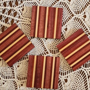 May include: Four square wooden coasters with a striped pattern of light brown and dark red wood.