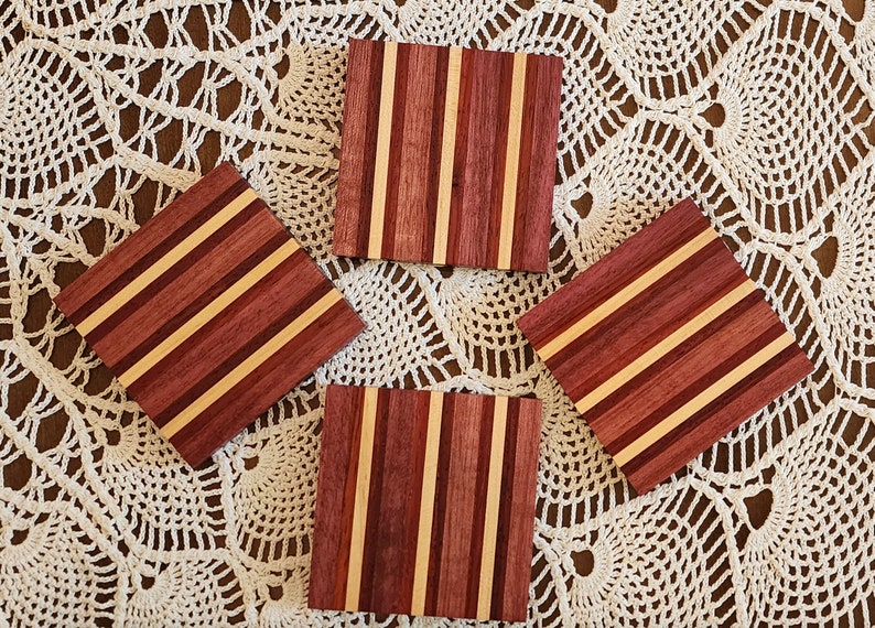 May include: Four square wooden coasters with a striped pattern of light brown and dark red wood.