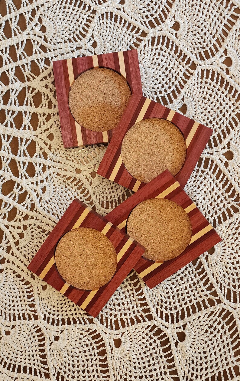 May include: Four square wooden coasters with cork inserts. The coasters have a red, brown, and light wood striped pattern.