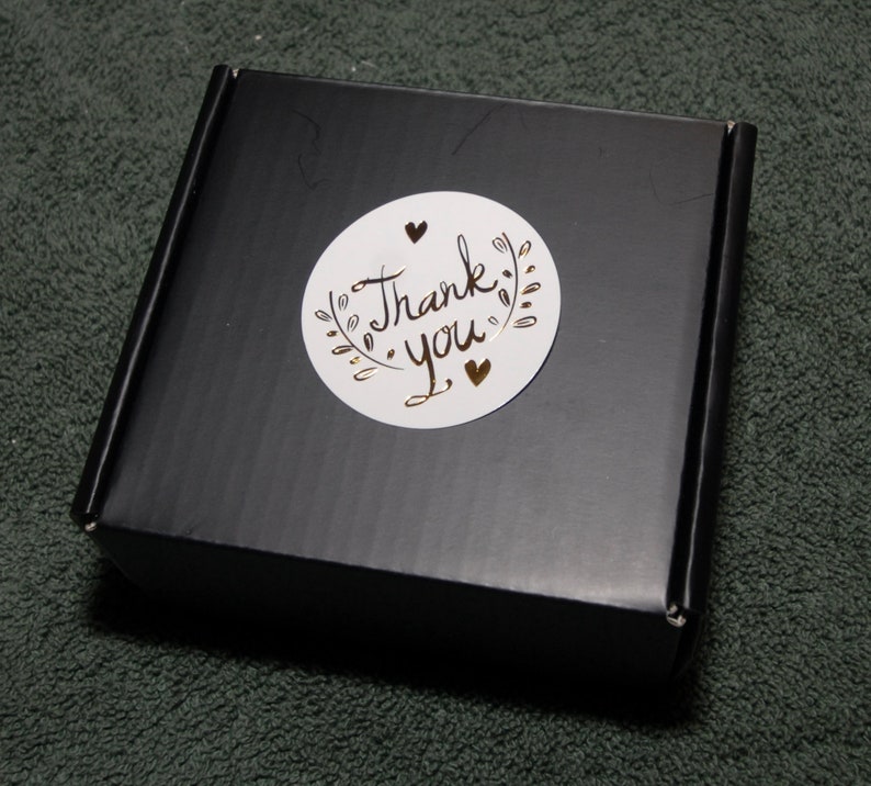May include: A black box with a white circle sticker that says "Thank you" in gold lettering with two gold hearts.