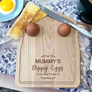 May include: A wooden breakfast serving tray with two egg cups and a space for toast. The tray is engraved with the text "Mummy's Dippy Eggs Love Amy & Kate xx".