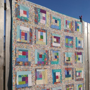 Op de afbeelding: Een quilt met een patchwork-ontwerp met verschillende bloemenstoffen in tinten blauw, groen, paars en rood. De quilt is gemaakt van vierkanten met verschillende patronen en kleuren, wat een visueel interessant en ingewikkeld ontwerp creëert.