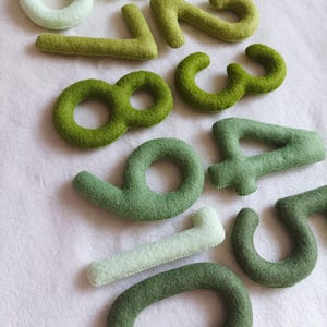 May include: Felt numbers in shades of green and white, from zero to nine. The numbers are arranged in a random order.