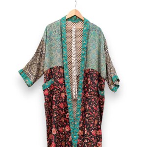 May include: A long-sleeved kimono robe featuring a patchwork design with a black floral lower section, a teal and brown patterned upper section, and a beige polka-dot interior lining. The garment has a teal trim along the front opening and cuffs.