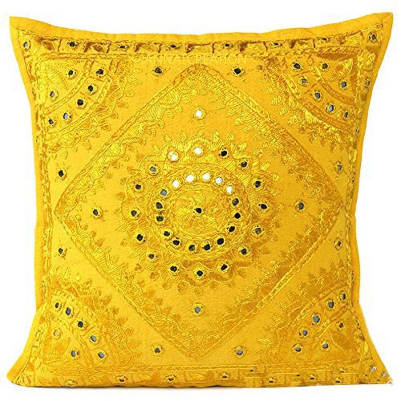 Puede incluir: Una funda de coj&iacute;n cuadrada de color amarillo con intrincados bordados tonales en patrones de diamantes y c&iacute;rculos. El dise&ntilde;o est&aacute; adornado con numerosos espejos circulares peque&ntilde;os y reflectantes incrustados en la tela.