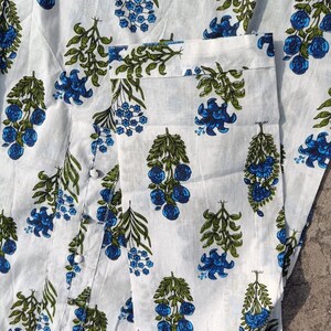Puede incluir: Tela de algod&oacute;n blanca con estampado floral azul y verde. La tela tiene un brillo sutil y una textura suave.