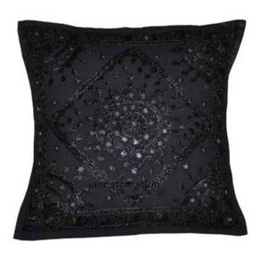 Puede incluir: Una funda de coj&iacute;n cuadrada de color negro con intrincados bordados negros y peque&ntilde;os espejos reflectantes dispuestos en un patr&oacute;n de diamante central. La superficie presenta costuras detalladas y el texto jannatcreation.