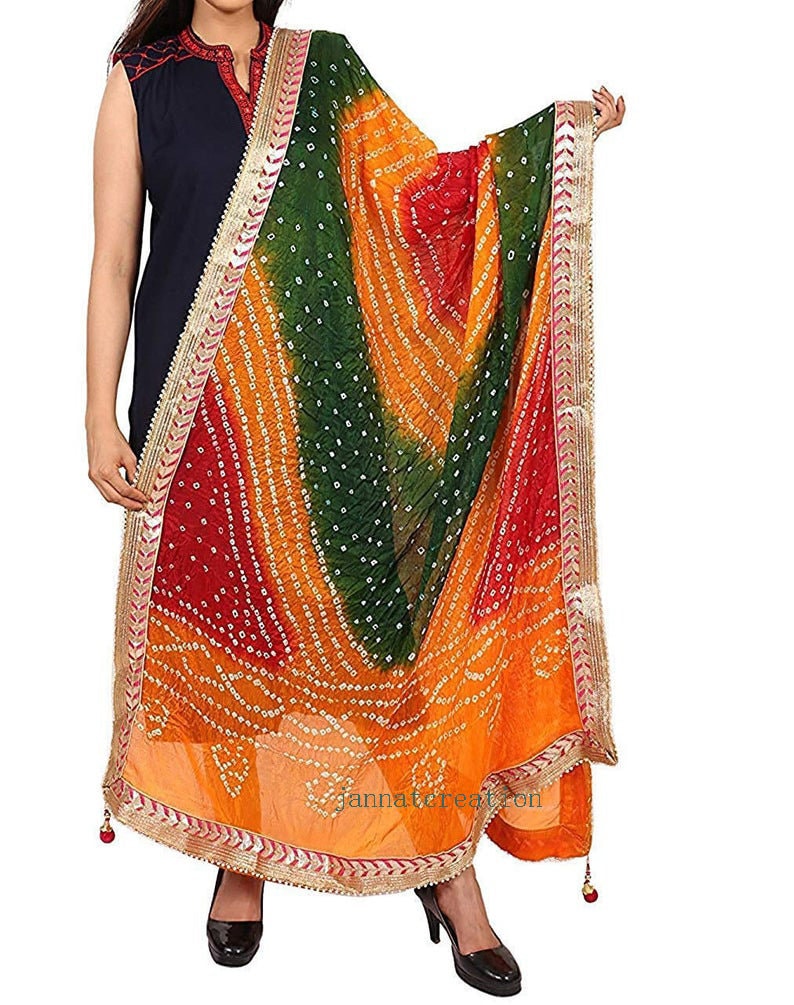 May include: A colorful dupatta with a bandhani pattern in shades of red, green, and orange. The scarf has a gold border with intricate detailing and small tassels. The fabric is draped, showcasing the vibrant colors and design.