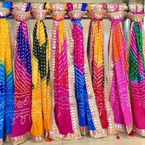 May include: A display of colorful, patterned scarves. The scarves are in shades of yellow, blue, purple, pink, orange, and green. Each scarf has a decorative gold trim. The scarves are hanging from a metal rod.