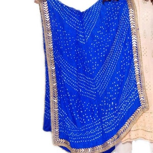 May include: A vibrant blue dupatta with a white dotted pattern and gold trim. The scarf is draped, showcasing its design and texture. The dupatta is a traditional Indian garment.