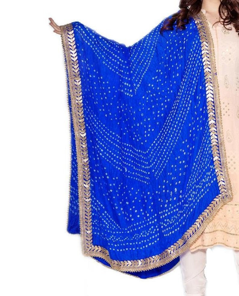 May include: A vibrant blue dupatta with a white dotted pattern and gold trim. The scarf is draped, showcasing its design and texture. The dupatta is a traditional Indian garment.