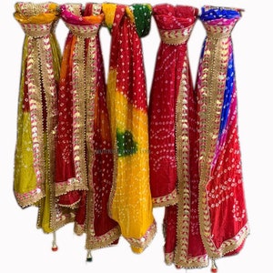 May include: A collection of colorful, patterned scarves hanging against a white background. The scarves feature a variety of colors, including yellow, red, green, and blue, with gold trim and tassels. The fabric has a dotted pattern.